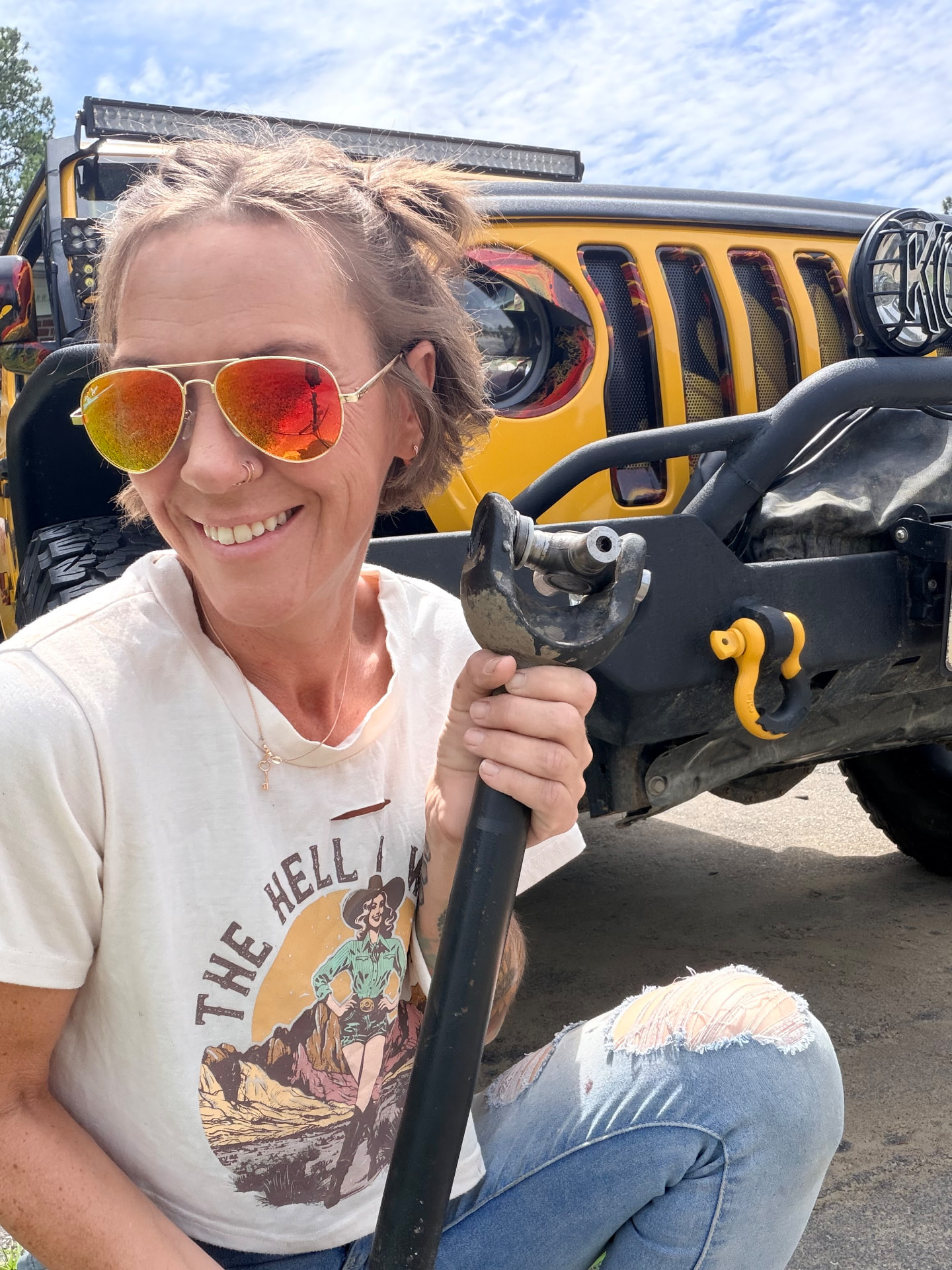 Melinda in front of her yellow Jeep holding recovery gear